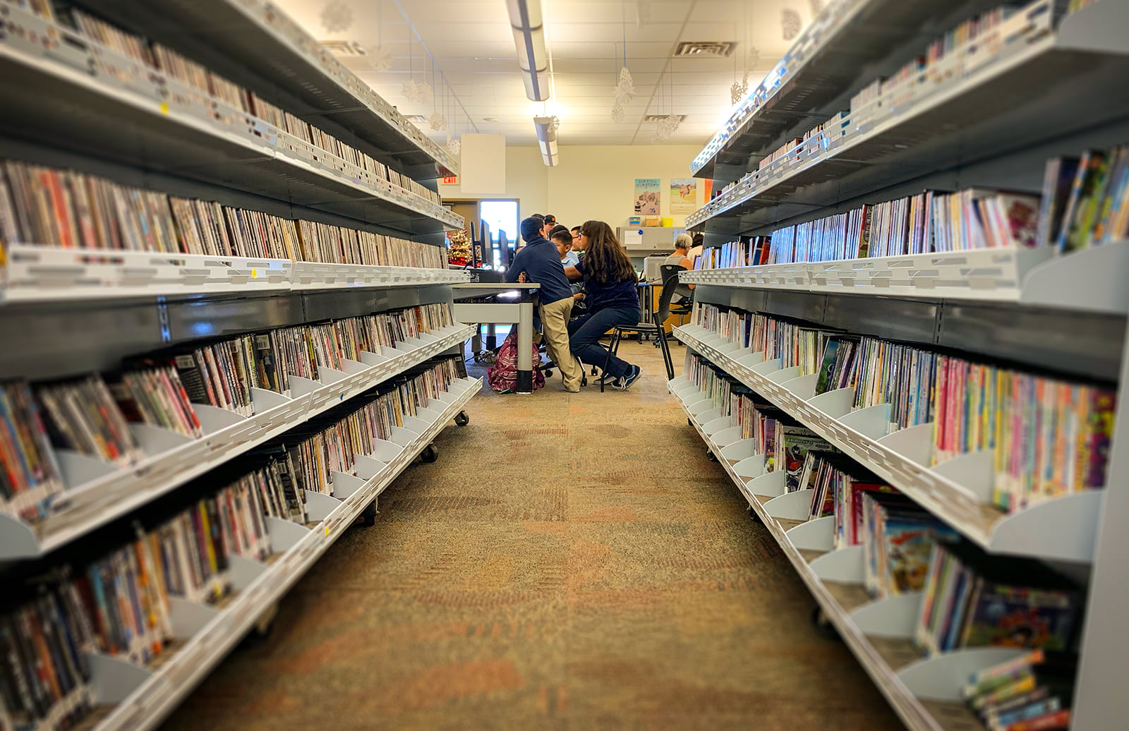 Photo of library shelves with children using computers in the background